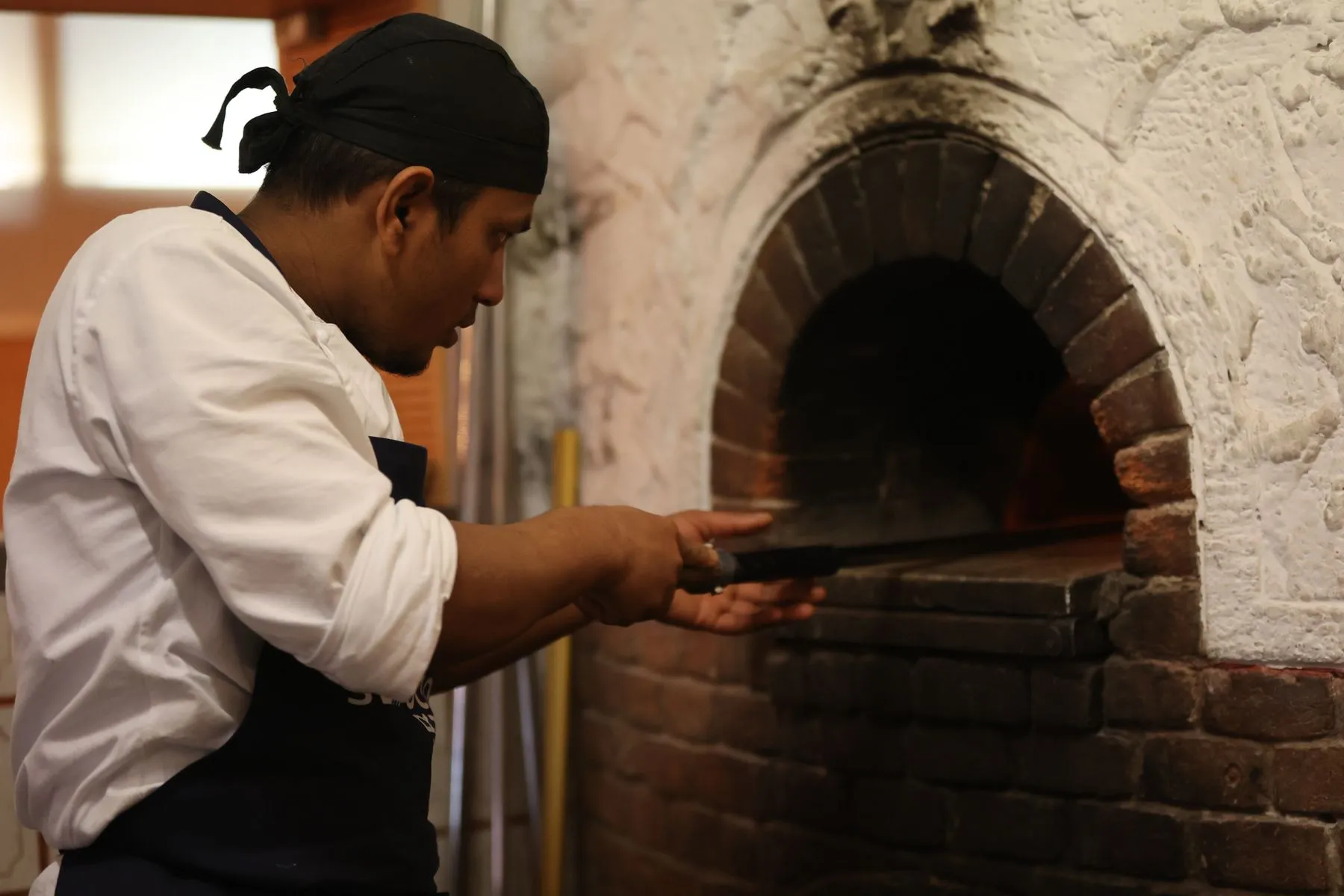 A pizzaiolo sliding a pizza into a brick oven