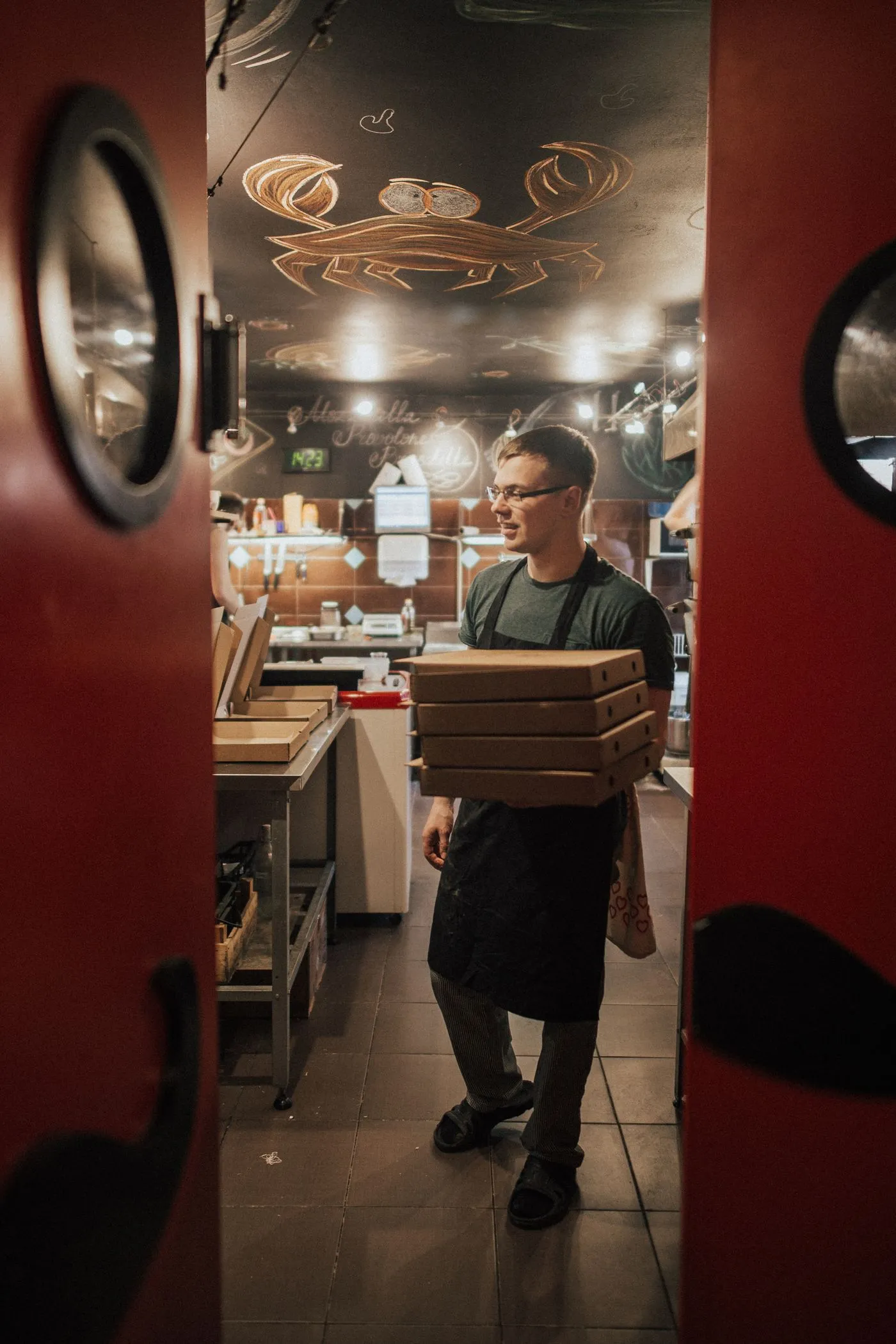 A pizzeria worker carrying a stack of boxes out the door for delivery